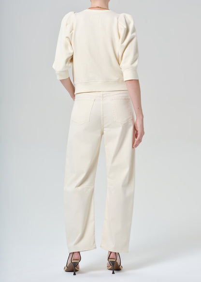 Person wearing a cream sweater and cream pants on a plain background