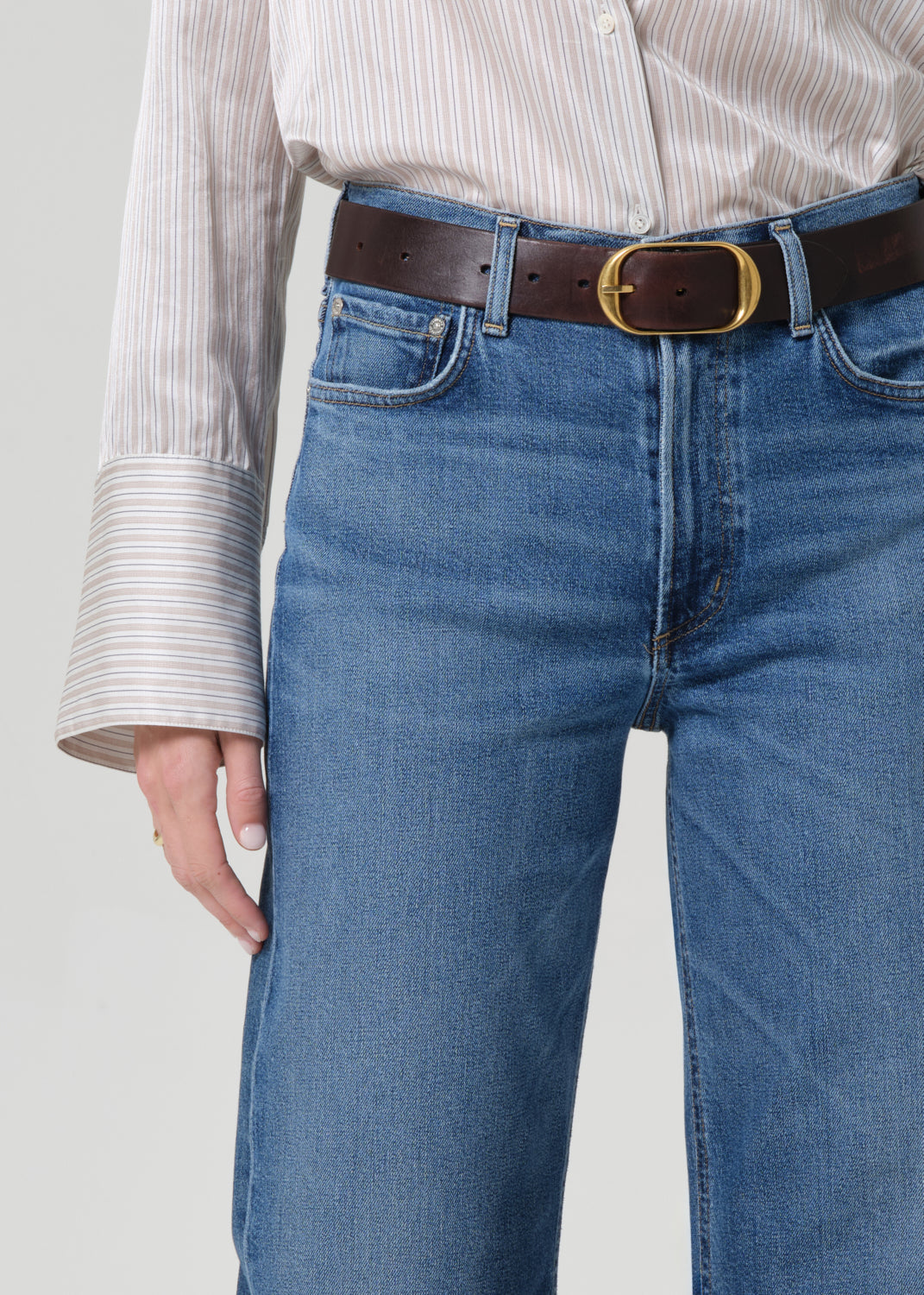 Person wearing a light-colored shirt and blue jeans on a grey background