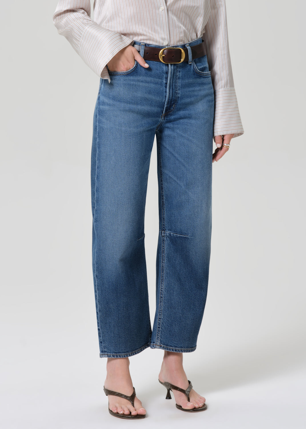 Person wearing a light-colored shirt and blue jeans on a grey background