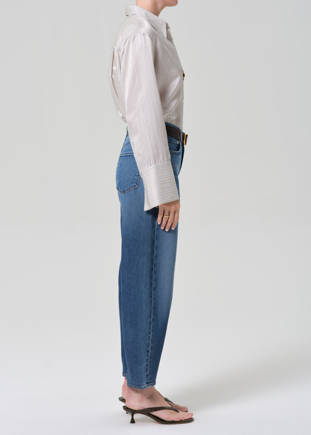 Person wearing a light-colored shirt and blue jeans on a grey background