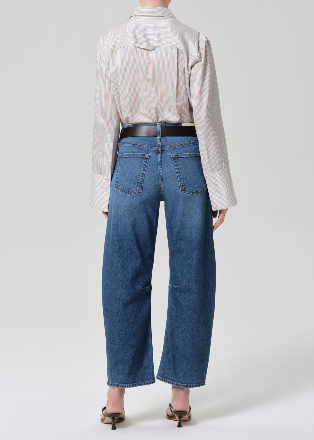 Person wearing a light-colored shirt and blue jeans on a grey background