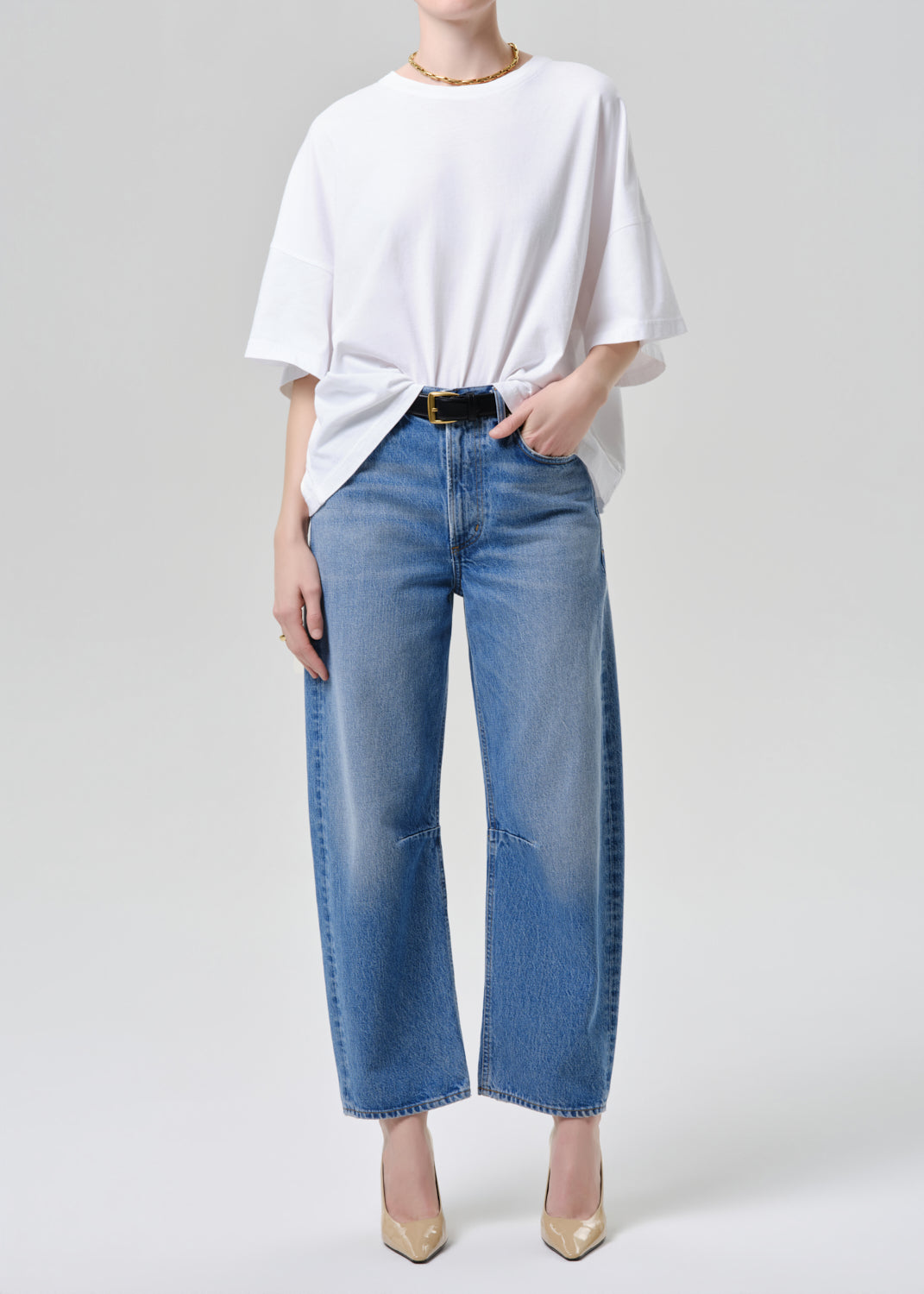 Person wearing a white oversized shirt and blue jeans on a grey background.