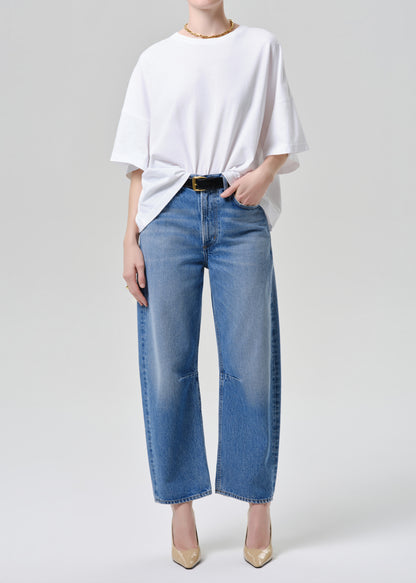 Person wearing a white oversized shirt and blue jeans on a grey background.