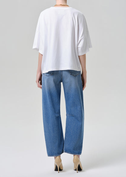 A model shown from the back wearing a white oversized short-sleeve t-shirt, blue wide-leg cropped jeans, and beige pointed-toe heels against a grey background.