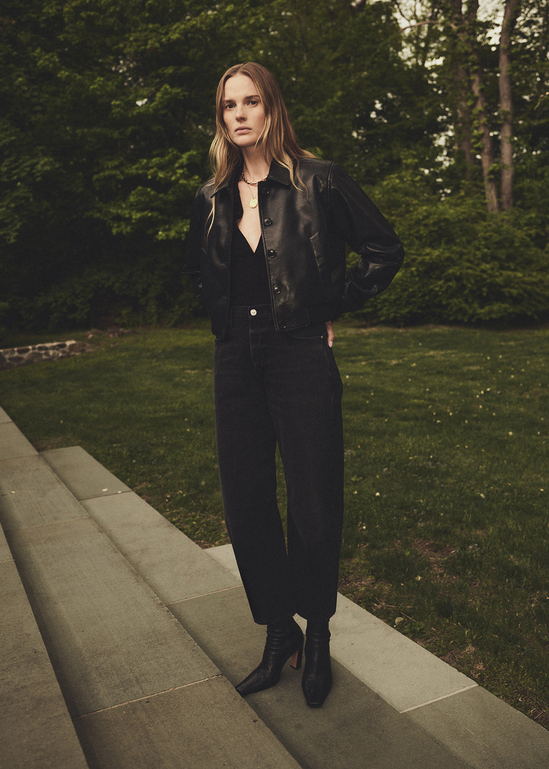Woman in a black outfit standing on stone steps with greenery in the background
