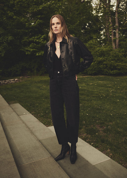Woman in a black outfit standing on stone steps with greenery in the background