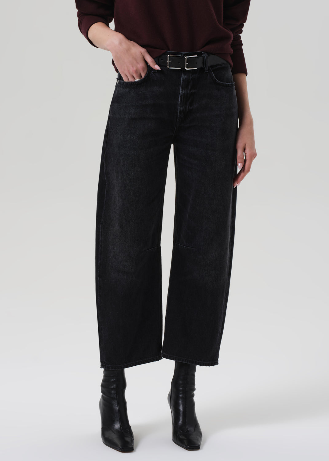 Person wearing a brown sweater and black jeans on a grey background