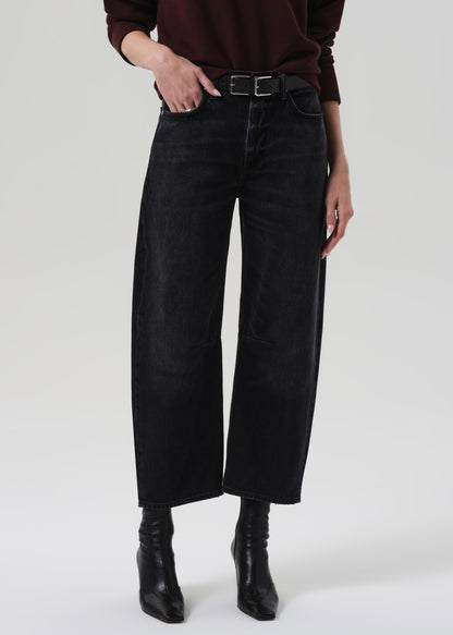 Person wearing a brown sweater and black jeans on a grey background