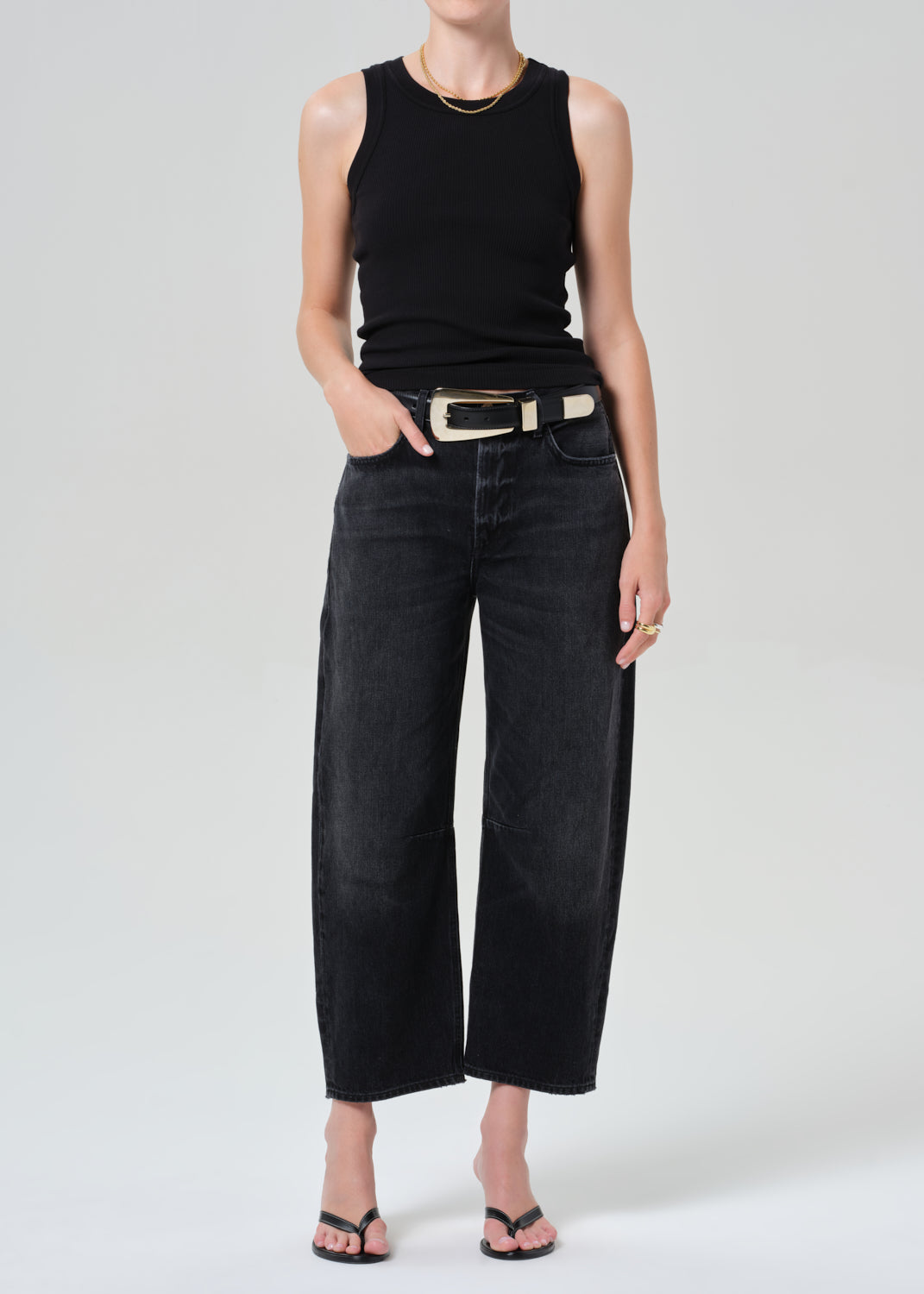 Person wearing a black sleeveless top and black jeans on a plain background