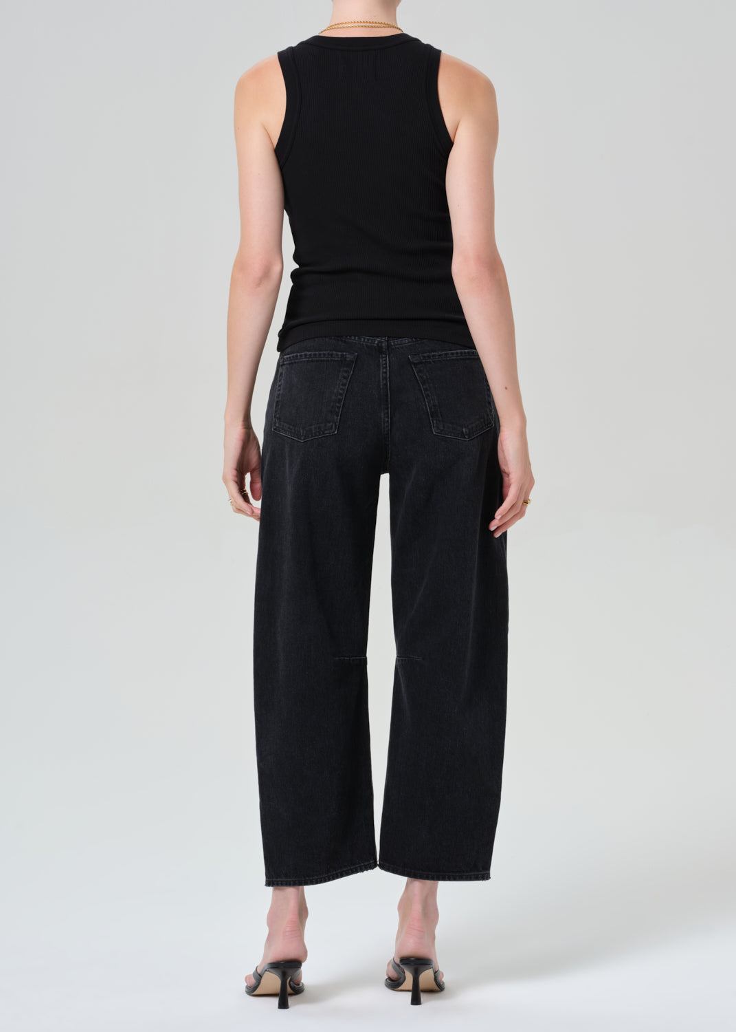 Person wearing a black sleeveless top and black jeans on a plain background