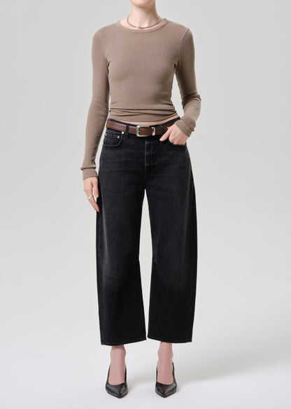 Person wearing a brown long-sleeve top and black wide-leg jeans on a light grey background