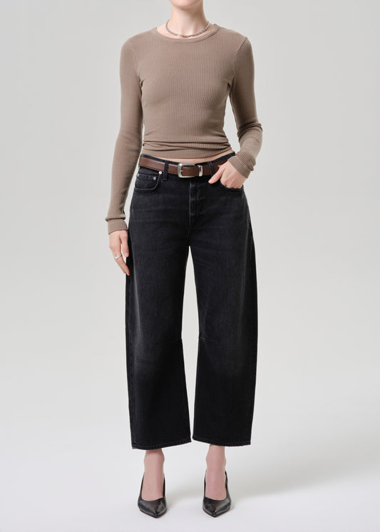 Person wearing a brown long-sleeve top and black wide-leg jeans on a light grey background