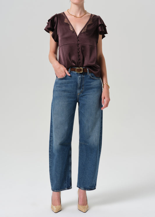 Person wearing brown top with blue pants on a grey background