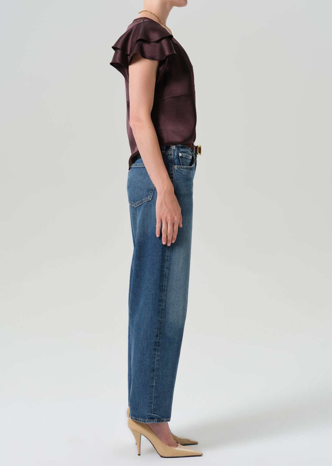 Person wearing brown top with blue pants on a grey background
