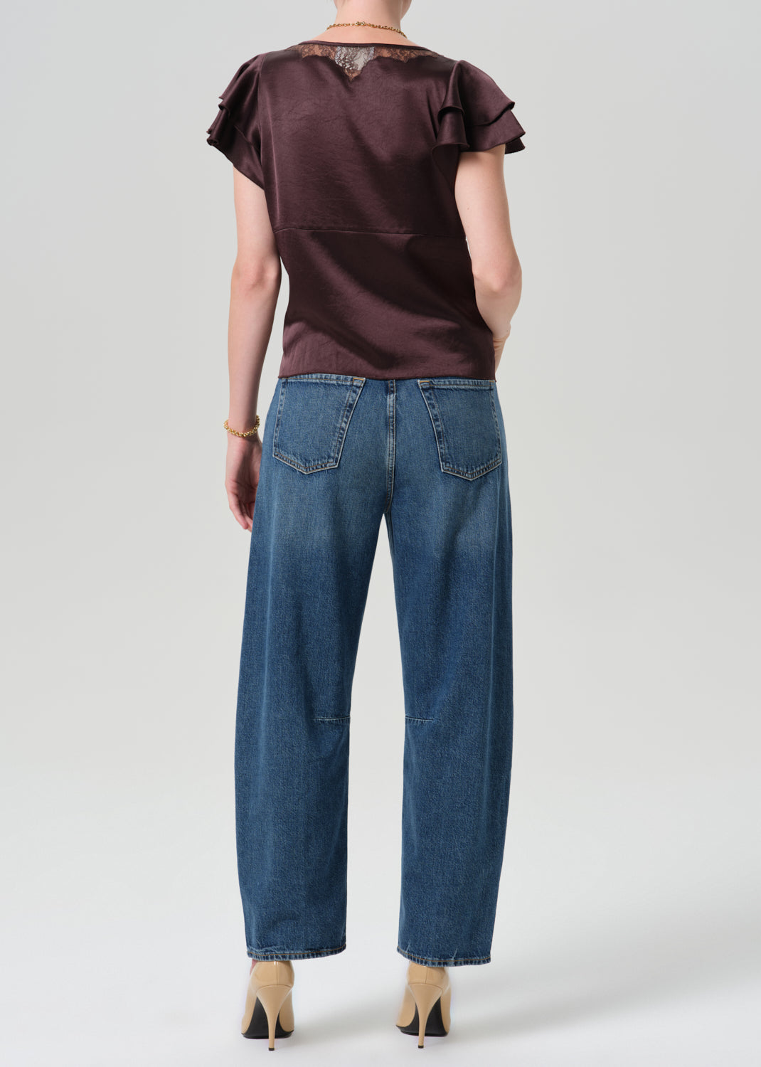 Person wearing brown top with blue pants on a grey background