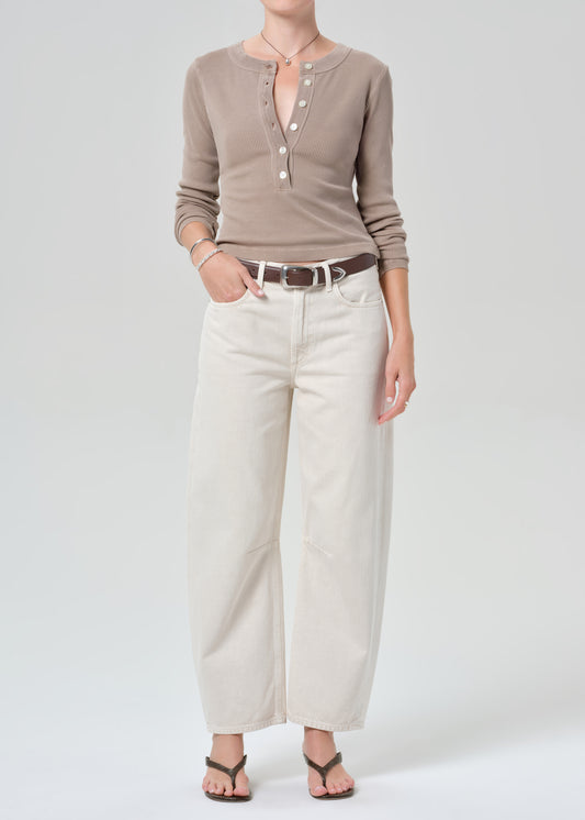 Person wearing a brown long-sleeve shirt and off-white jeans on a plain background