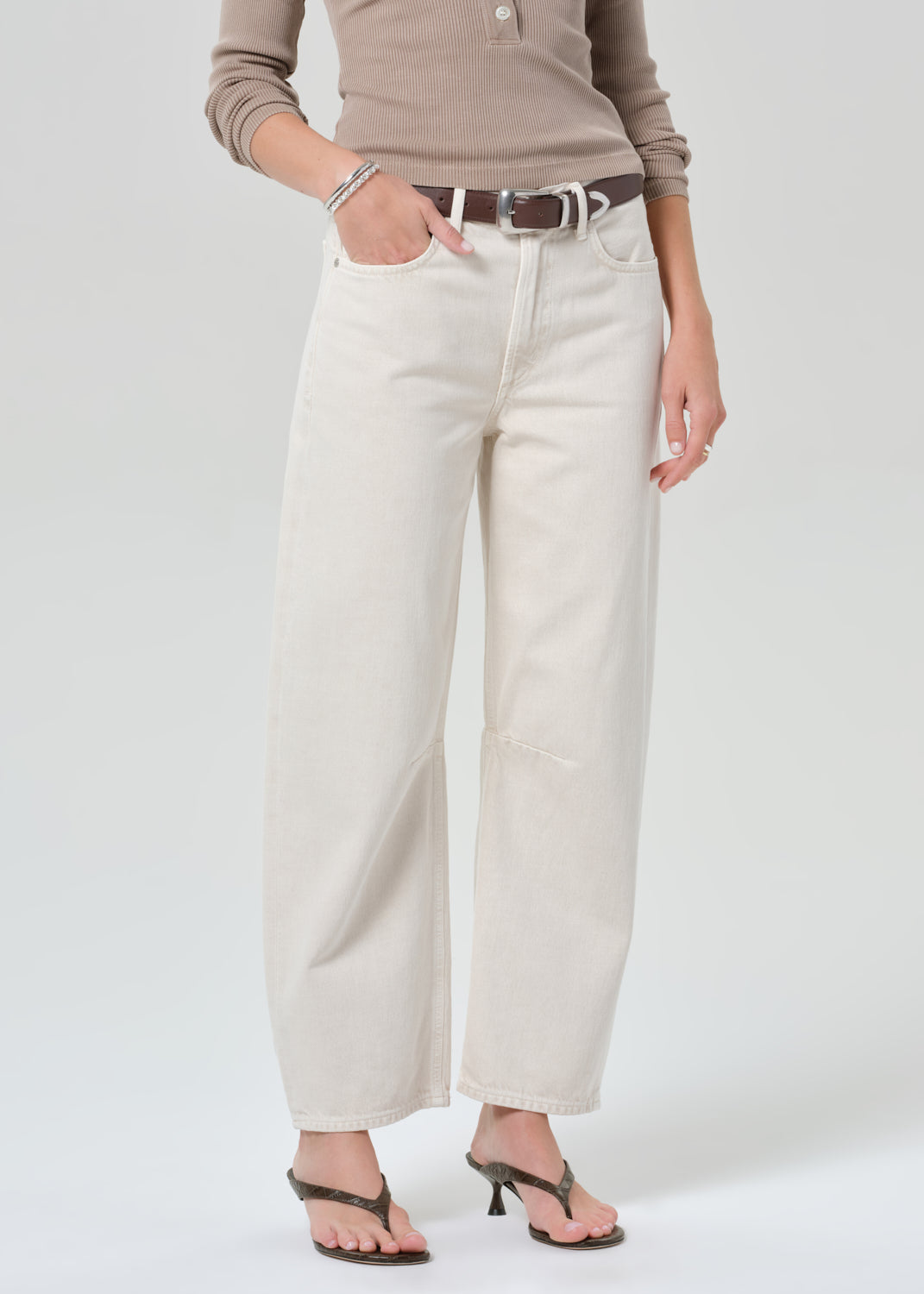 Person wearing a brown long-sleeve shirt and off-white jeans on a plain background