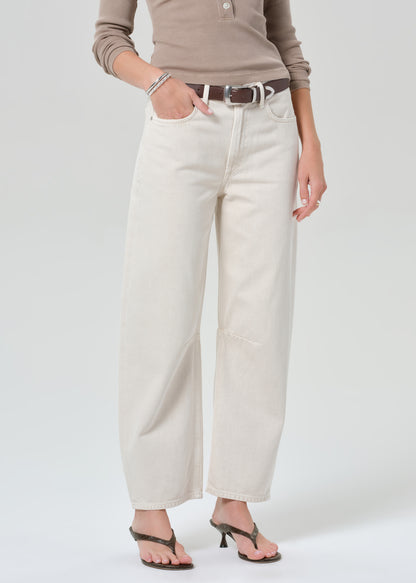 Person wearing a brown long-sleeve shirt and off-white jeans on a plain background