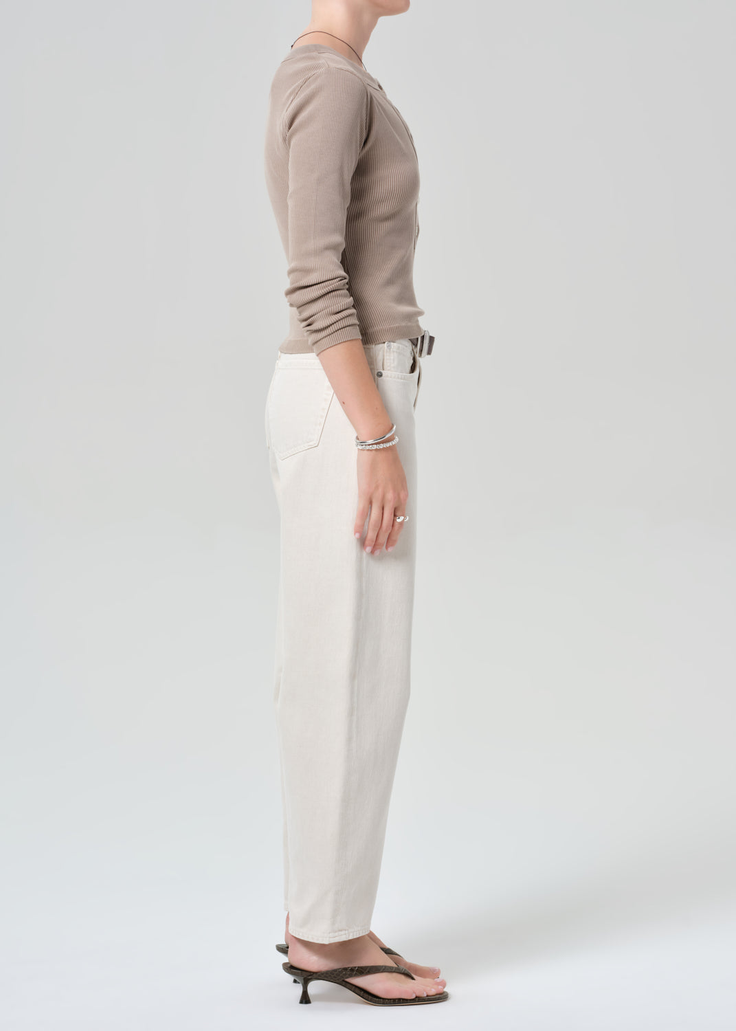 Person wearing a brown long-sleeve shirt and off-white jeans on a plain background