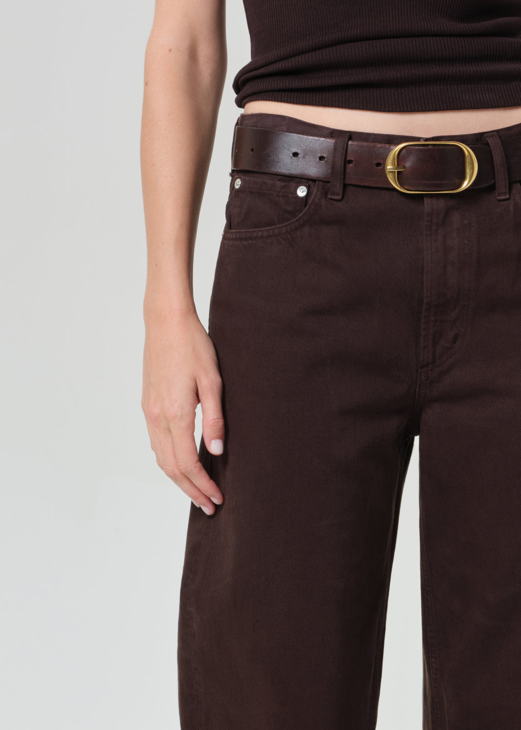 Person wearing a brown sleeveless top and brown pants on a plain background