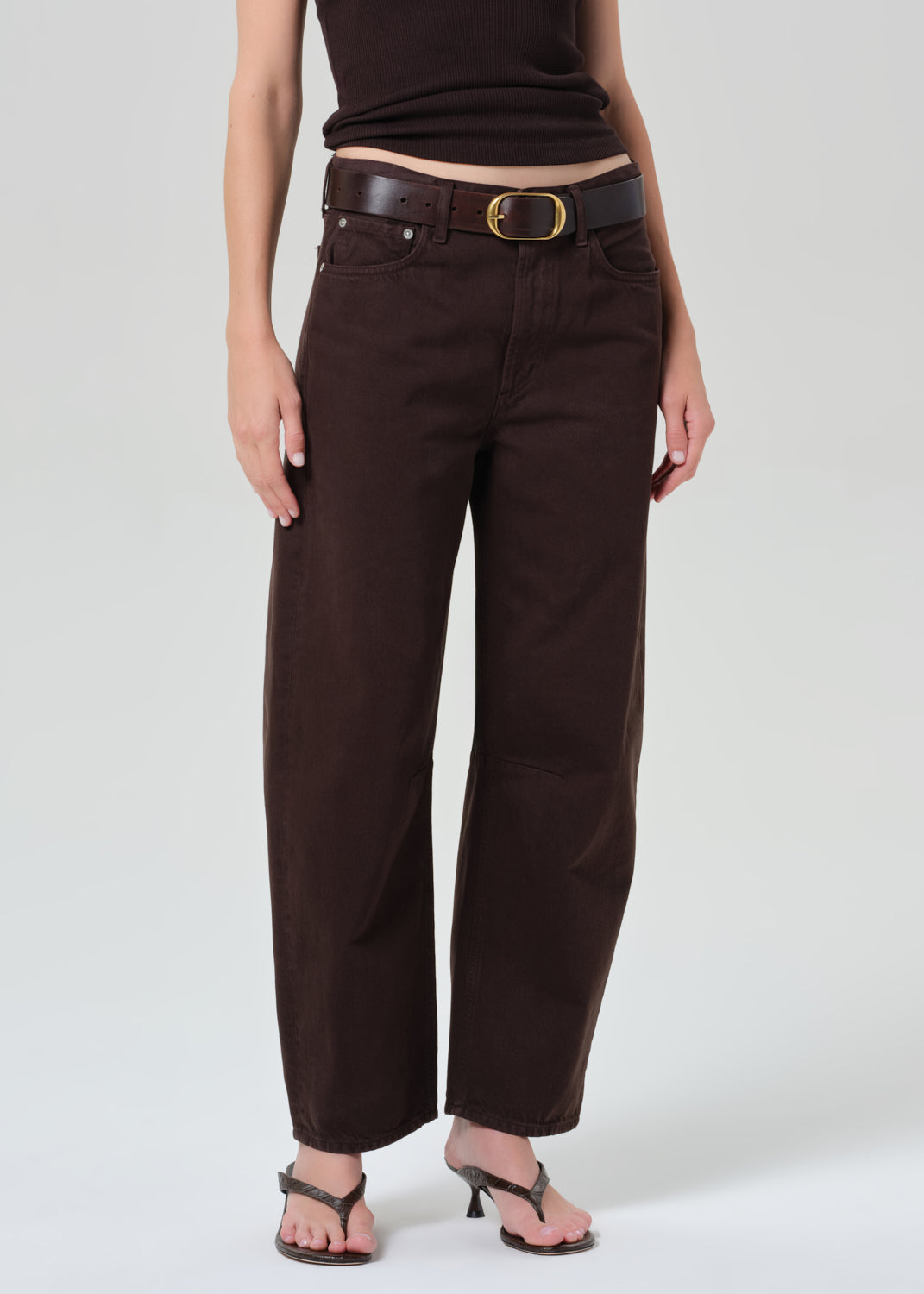 Person wearing a brown sleeveless top and brown pants on a plain background