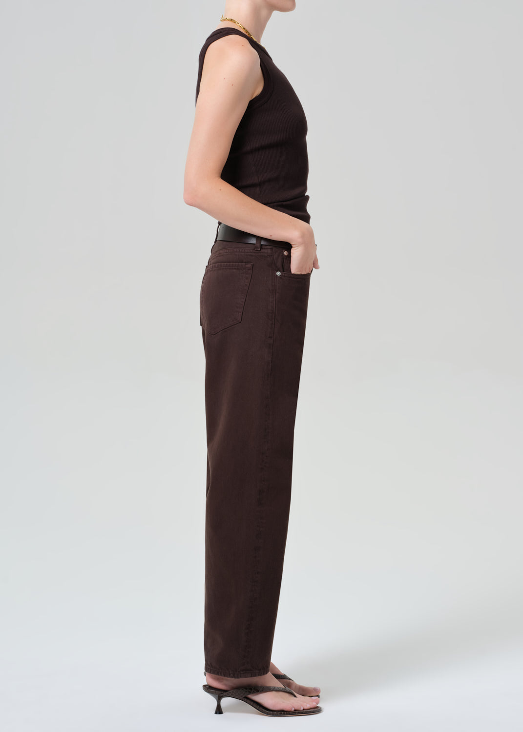 Person wearing a brown sleeveless top and brown pants on a plain background