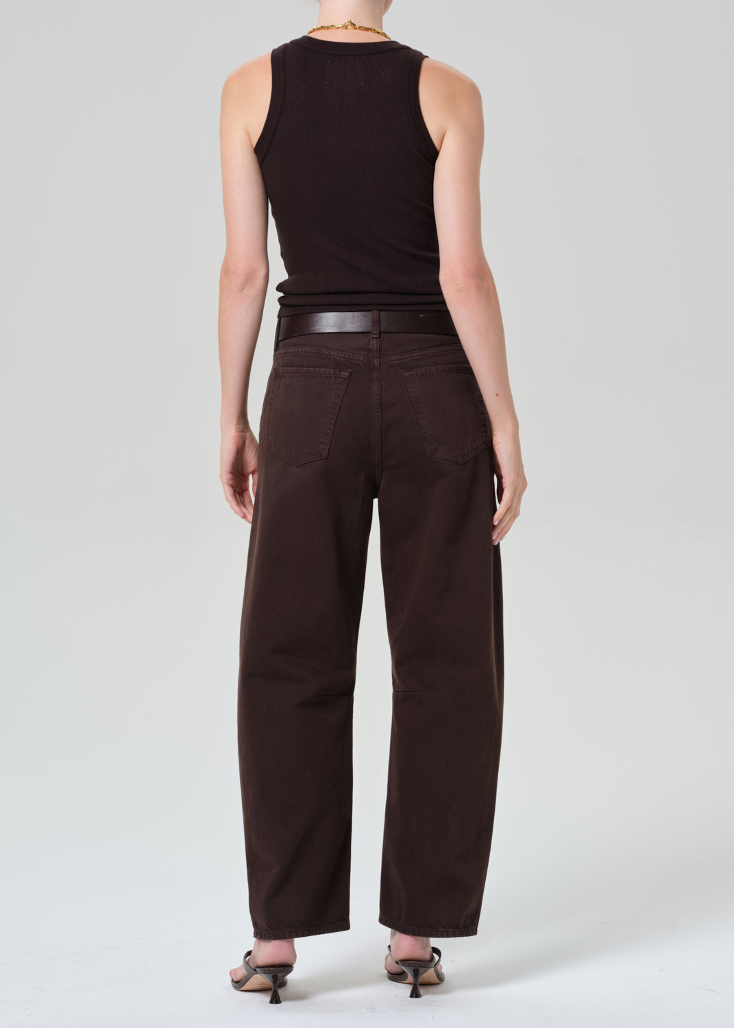 Person wearing a brown sleeveless top and brown pants on a plain background