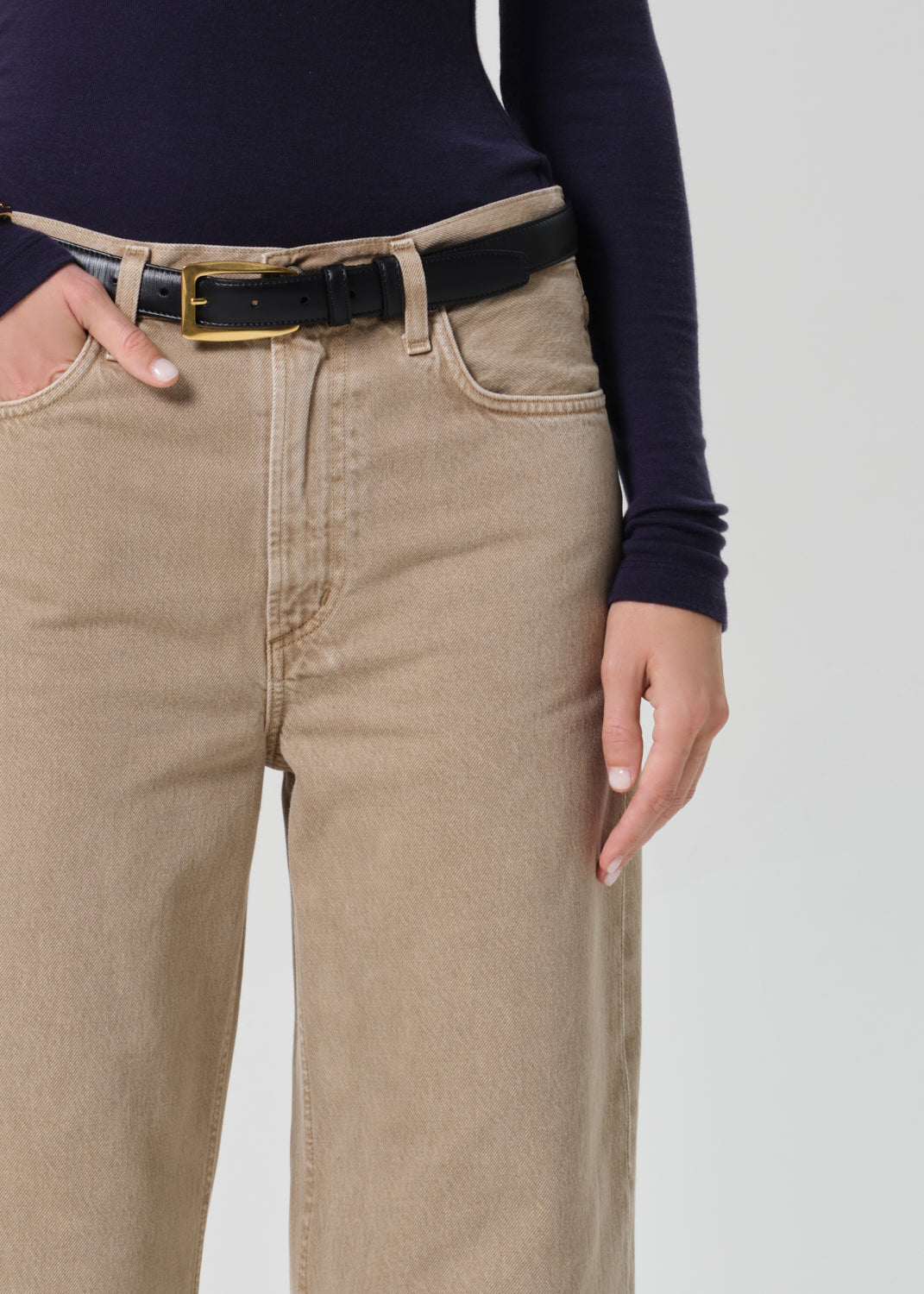 Person wearing a navy turtleneck and beige jeans on a grey background