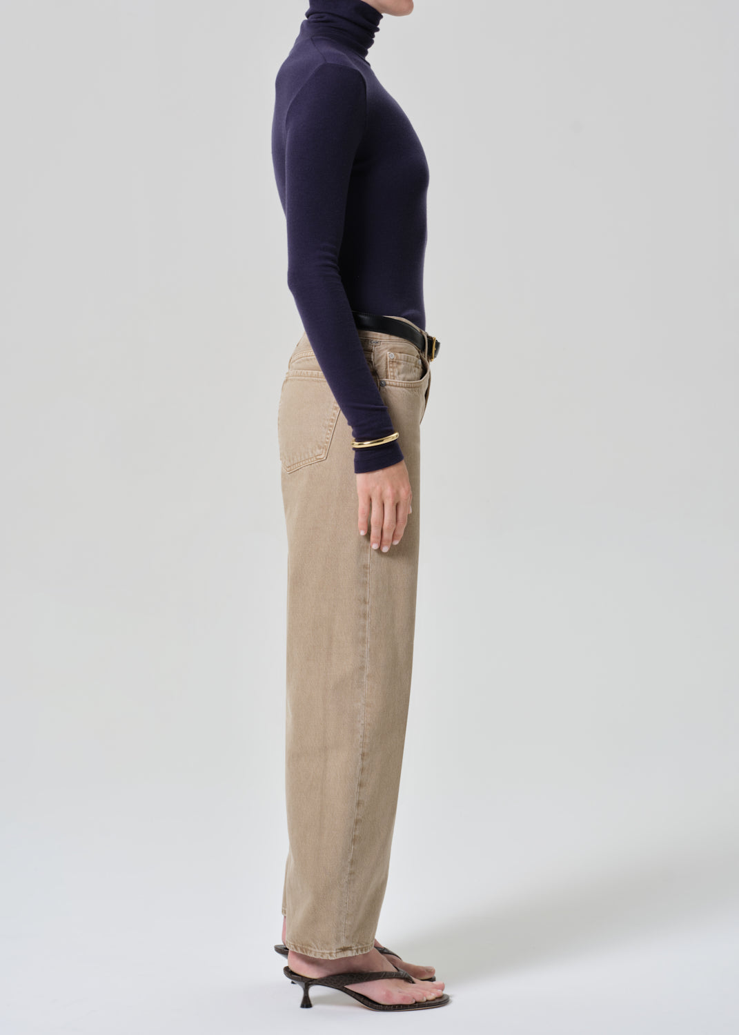 Person wearing a navy turtleneck and beige jeans on a grey background