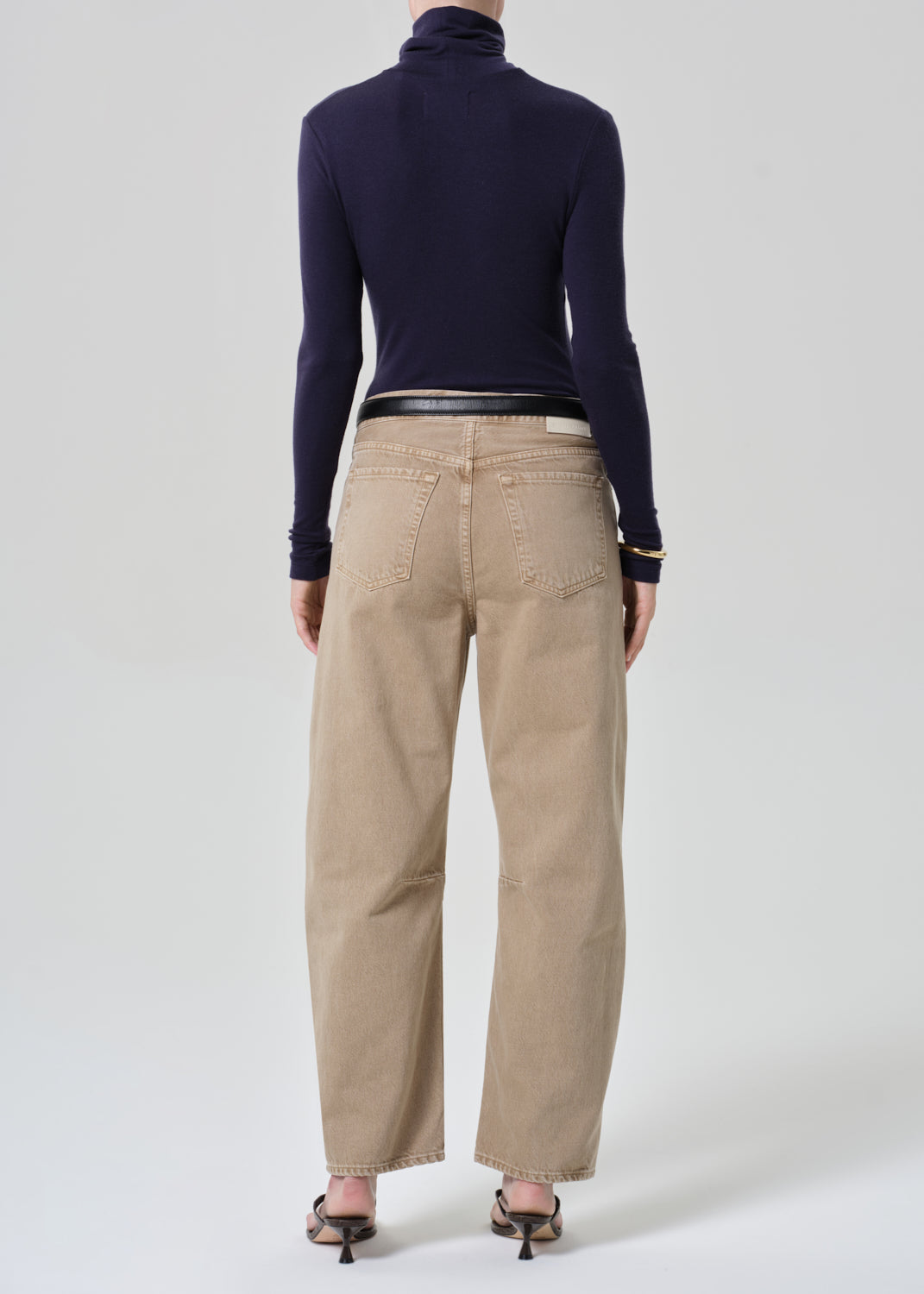Person wearing a navy turtleneck and beige jeans on a grey background