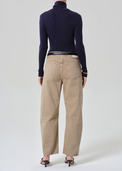 Person wearing a navy turtleneck and beige jeans on a grey background