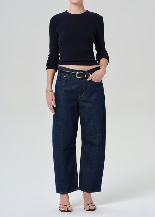 Person wearing a navy long sleeve top and dark blue jeans on a grey