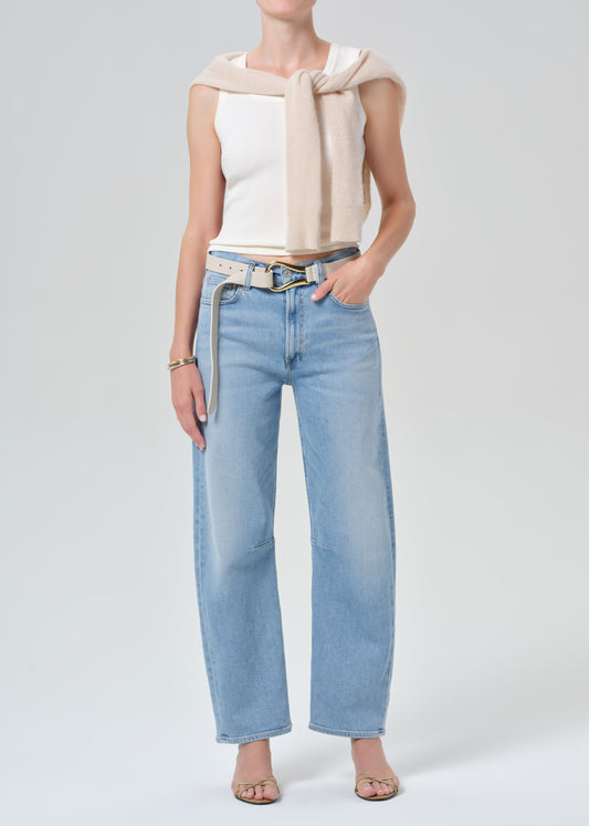 Person wearing a white sleeveless top and light blue jeans on a plain background