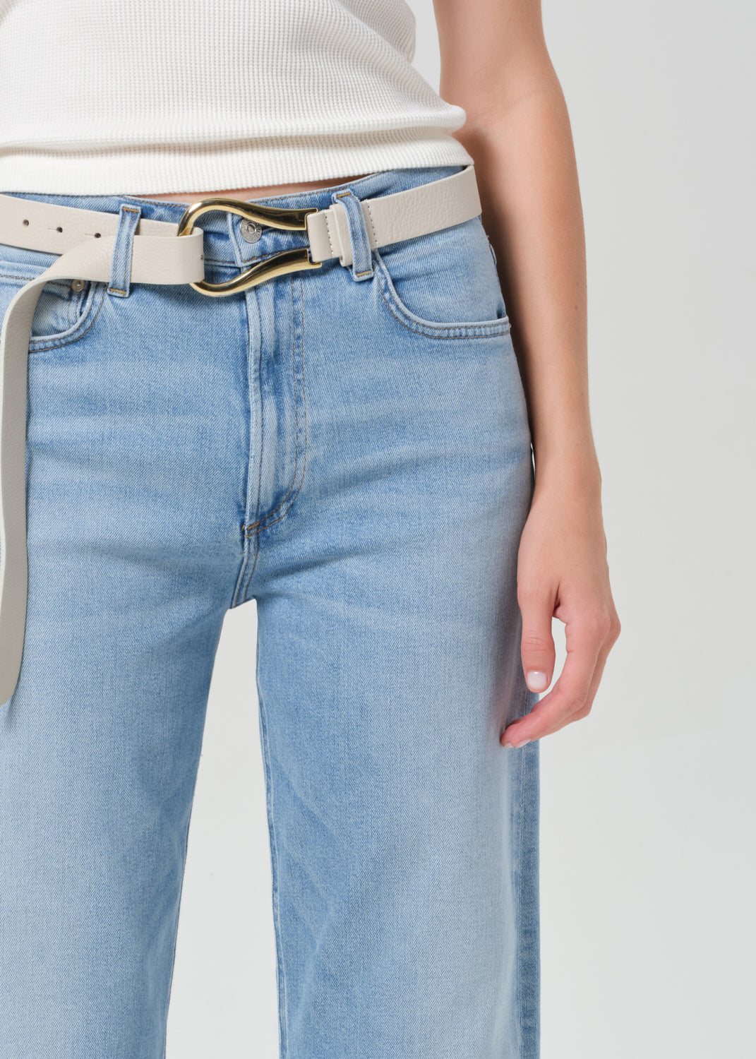 Light blue jeans with a beige belt on a plain background