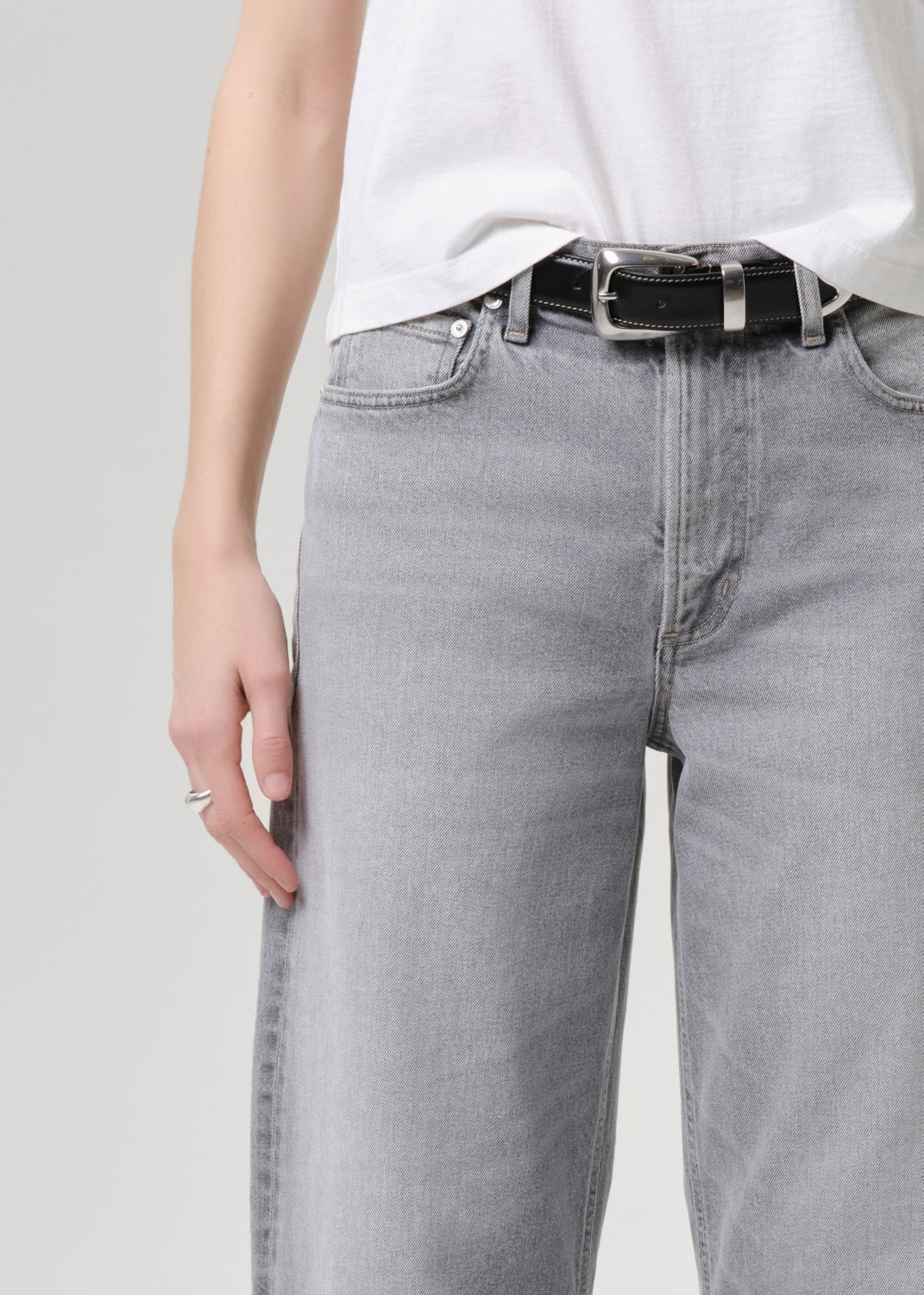 Person wearing grey jeans and a white shirt on a grey background