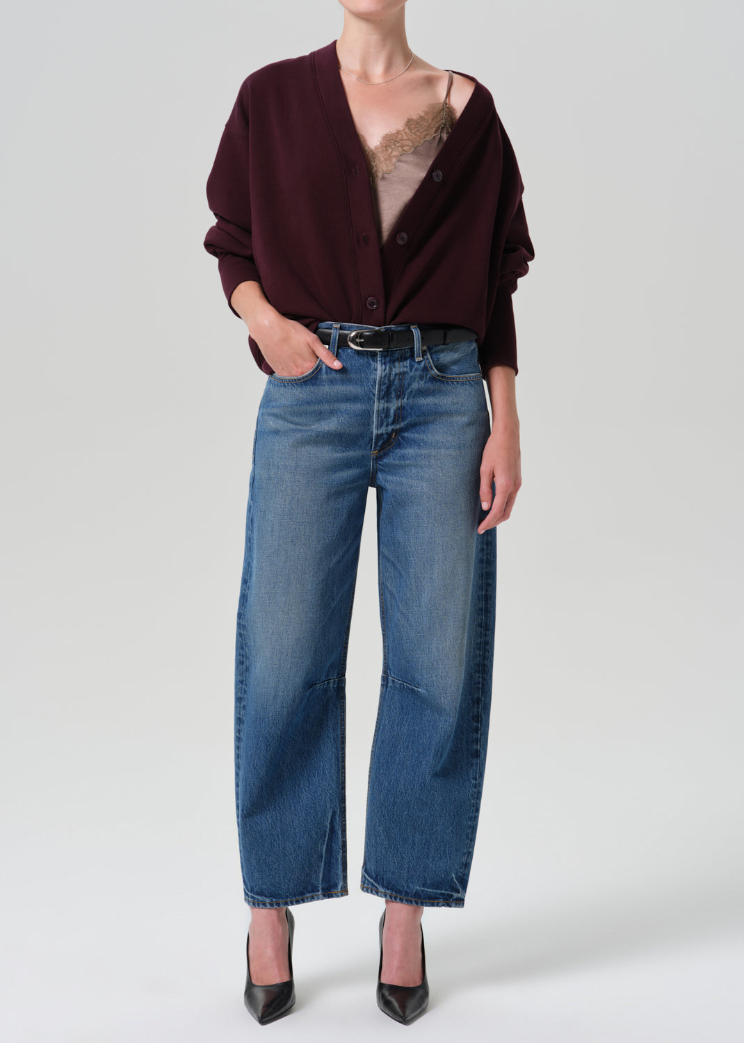 Person wearing burgundy cardigan and a blue pant on a grey background
