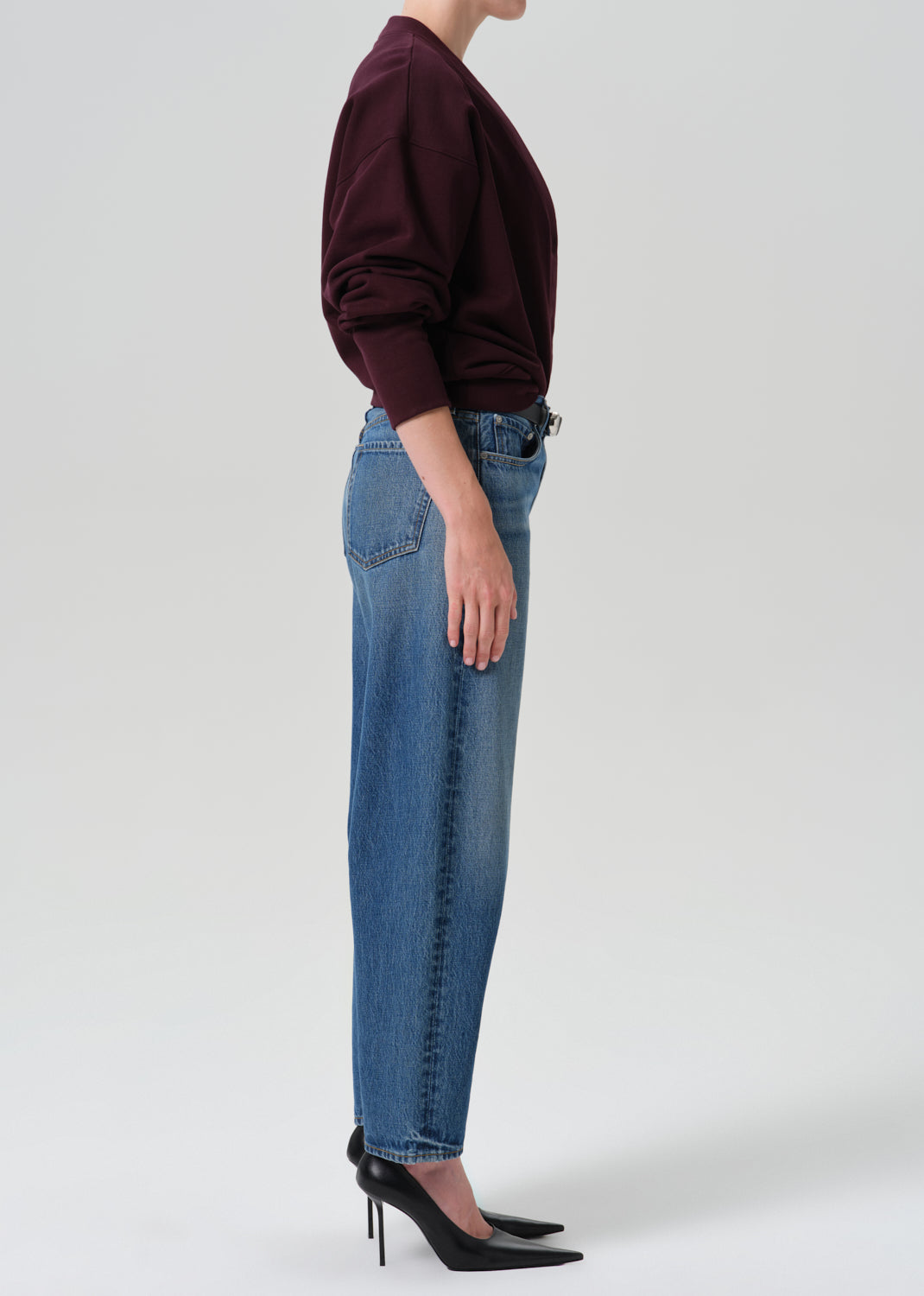 Person wearing burgundy cardigan and a blue pant on a grey background