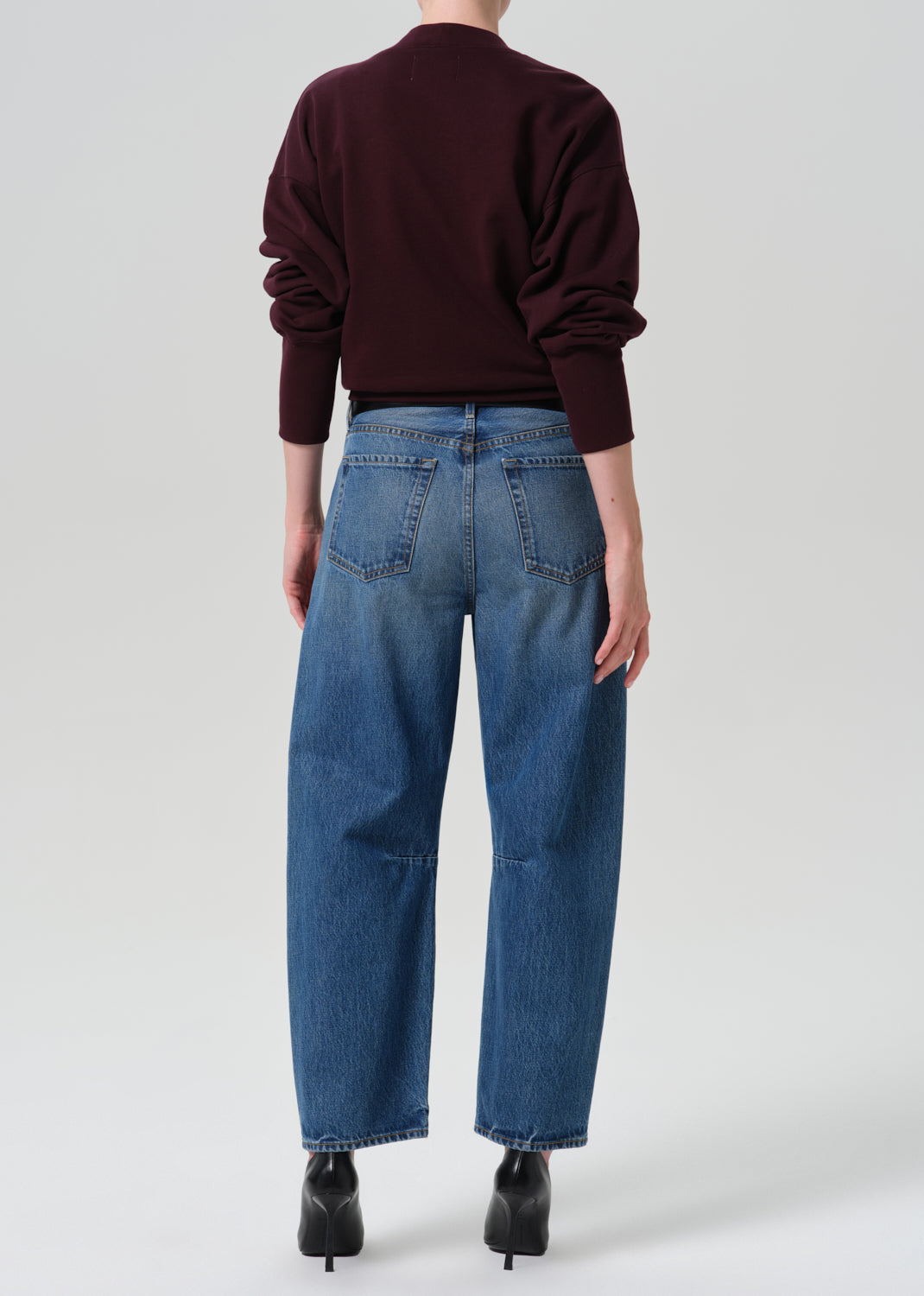 Person wearing burgundy cardigan and a blue pant on a grey background