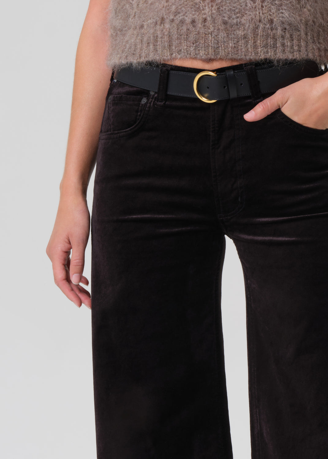 Person wearing a brown knitted sweater and black wide-leg pants on a grey background