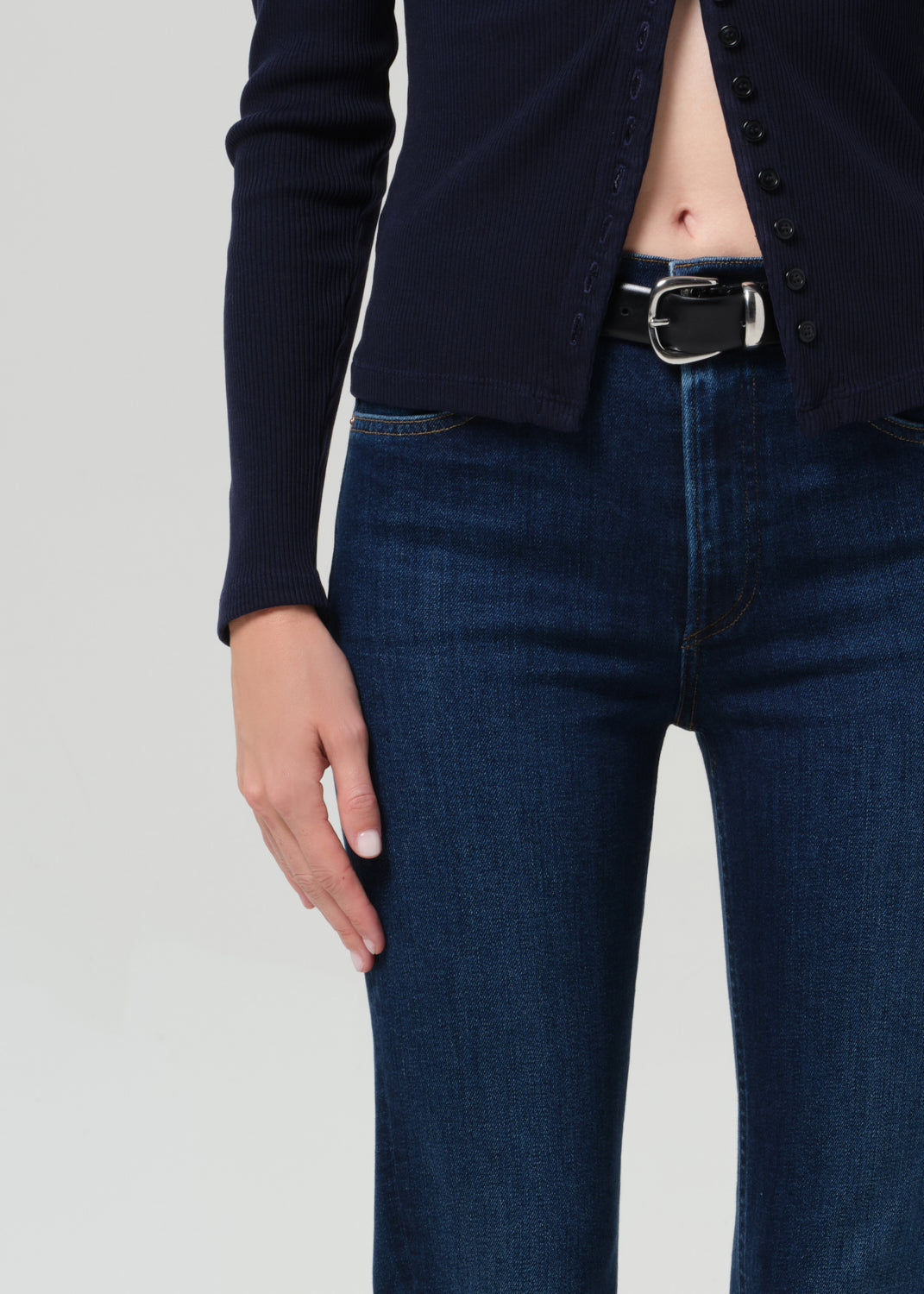 Person wearing a navy cardigan and dark blue jeans on a grey background