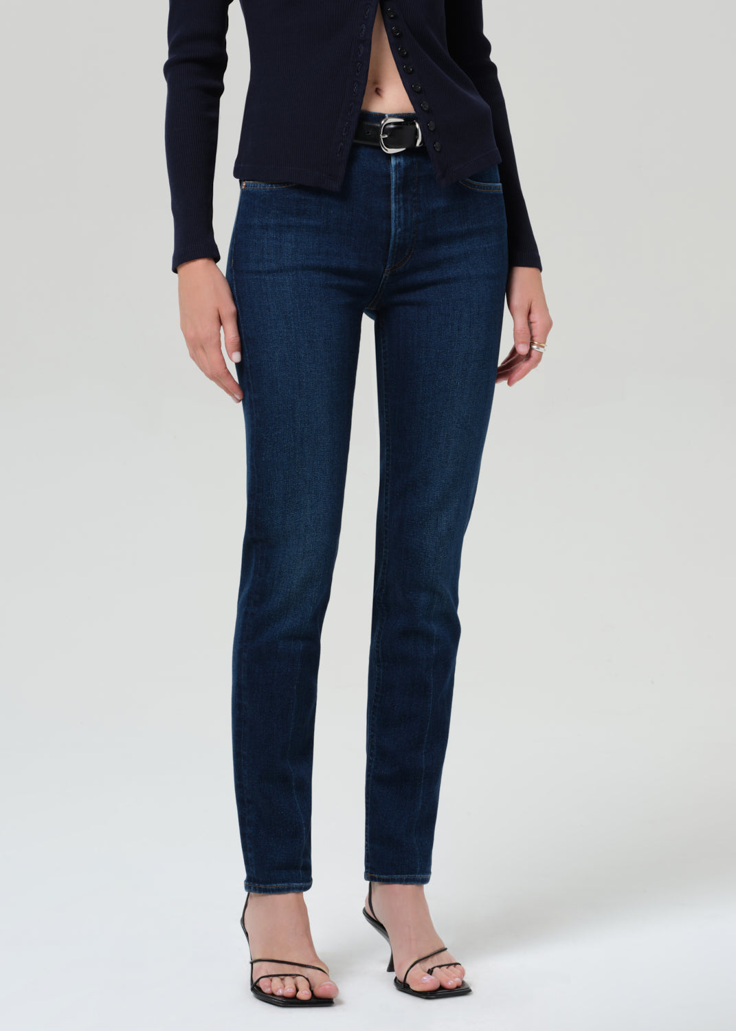 Person wearing a navy sweater and dark blue jeans on a grey background