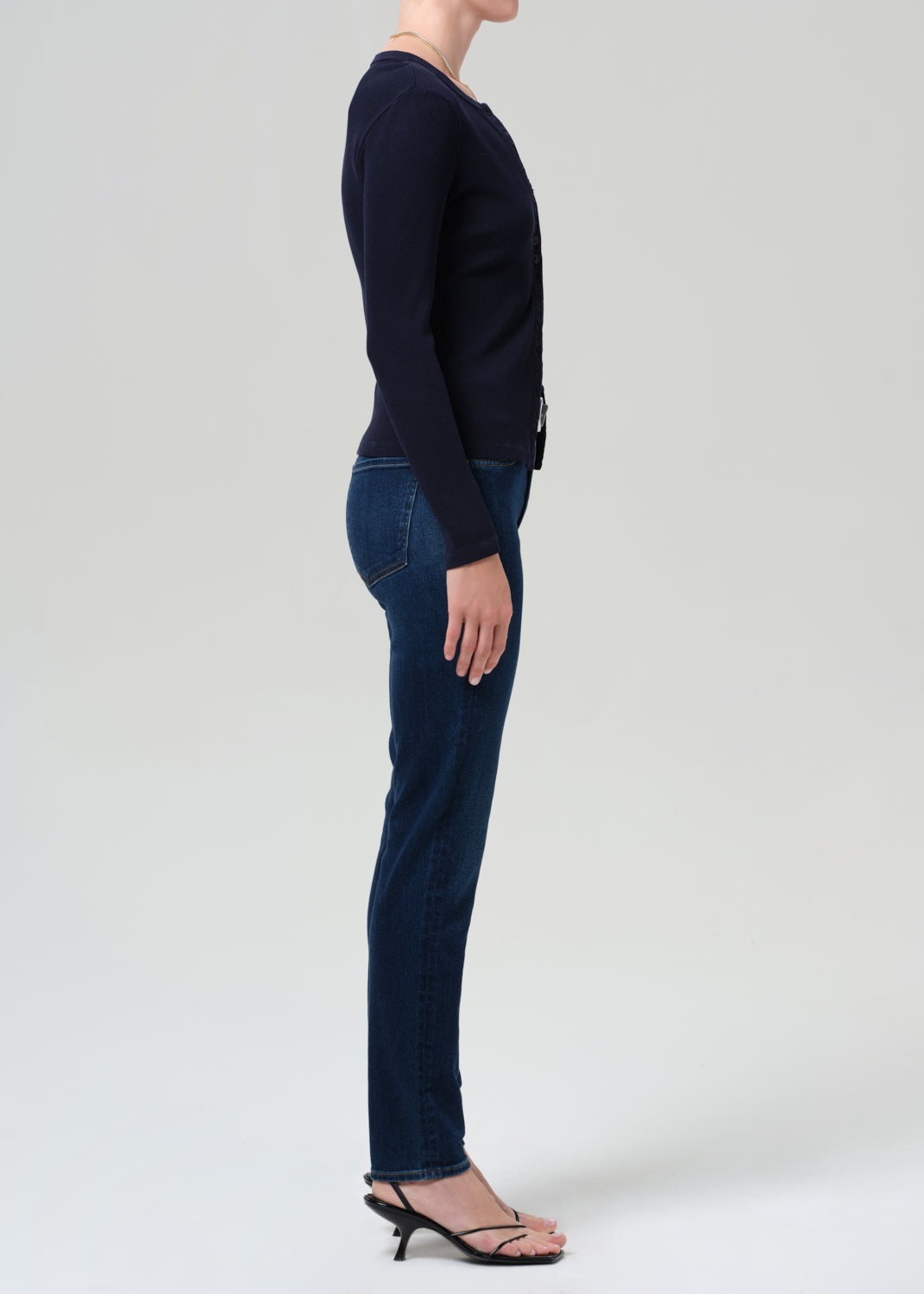 Person wearing a navy sweater and dark blue jeans on a grey background