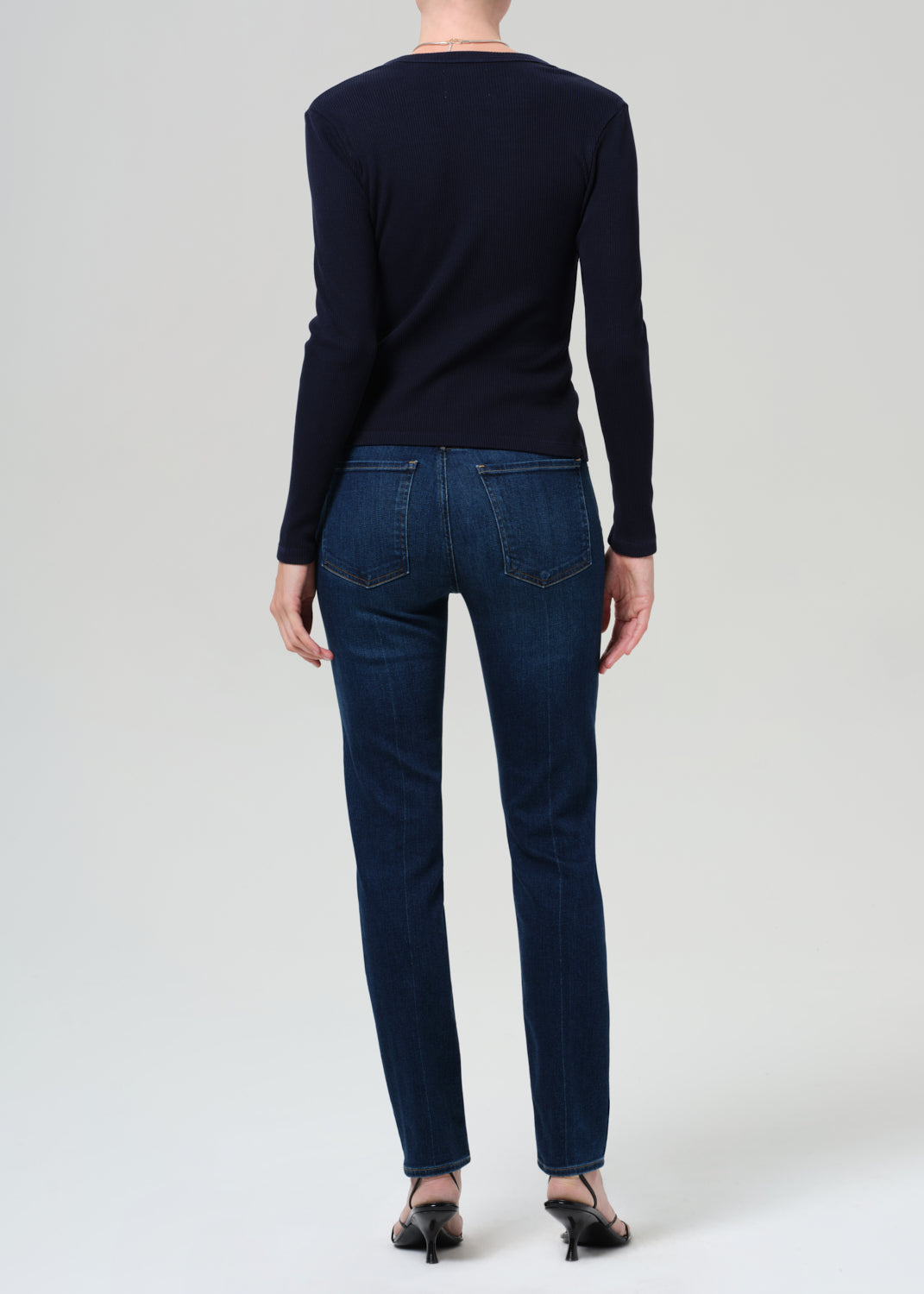 Person wearing a navy sweater and dark blue jeans on a grey background