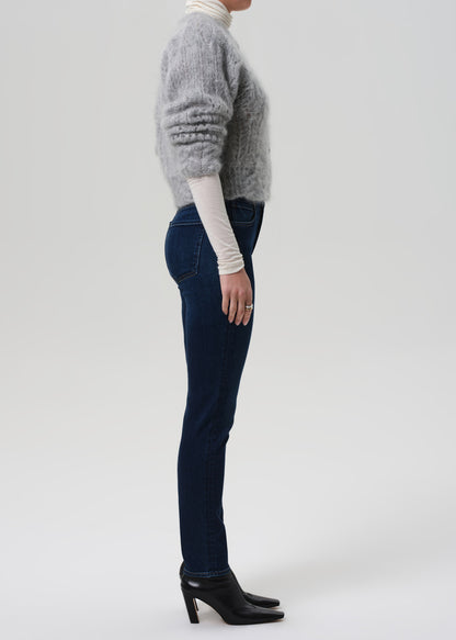 Person wearing a gray sweater, white turtleneck, dark jeans, and black shoes on a light gray background