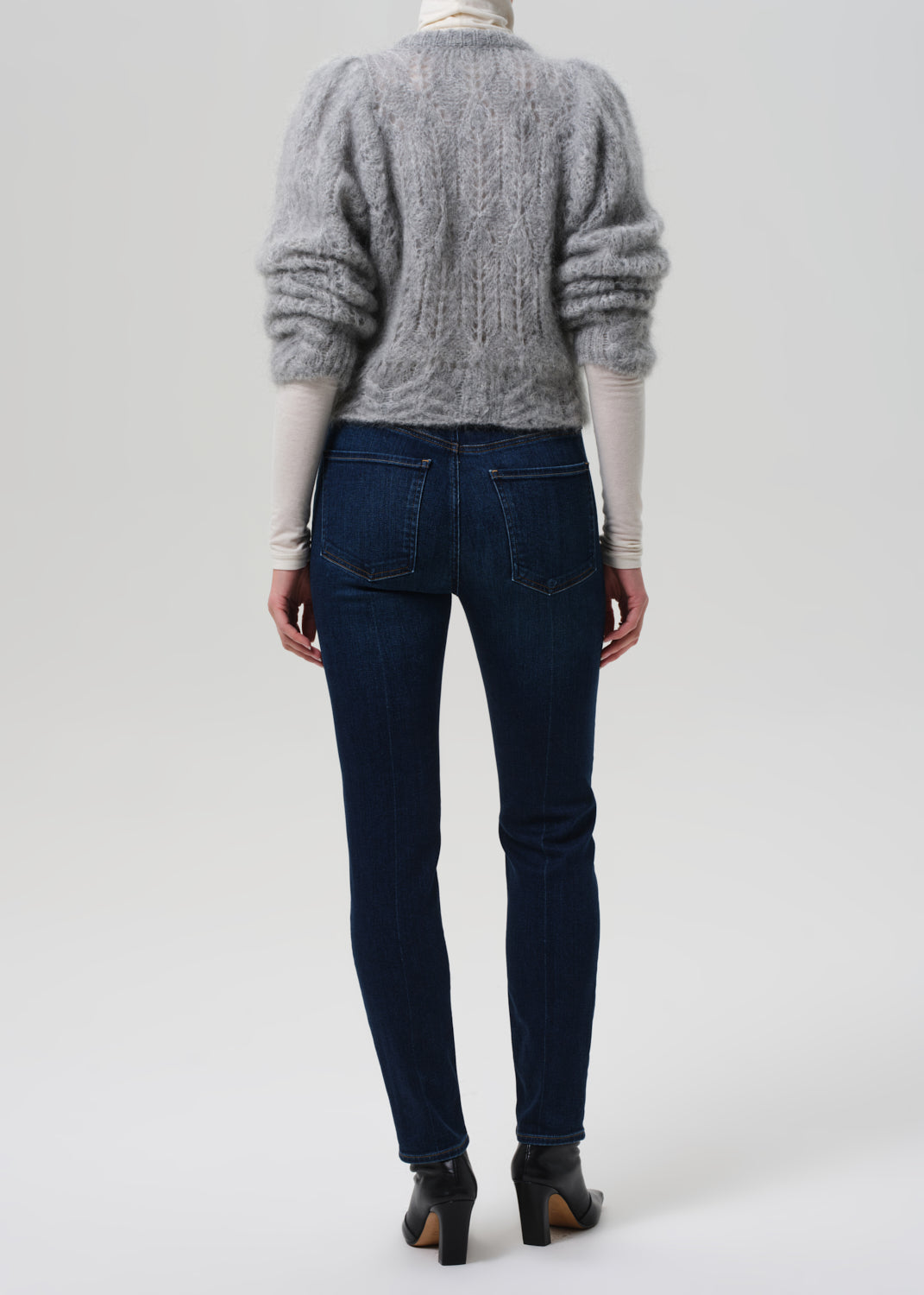Person wearing a gray sweater and dark blue jeans on a white background
