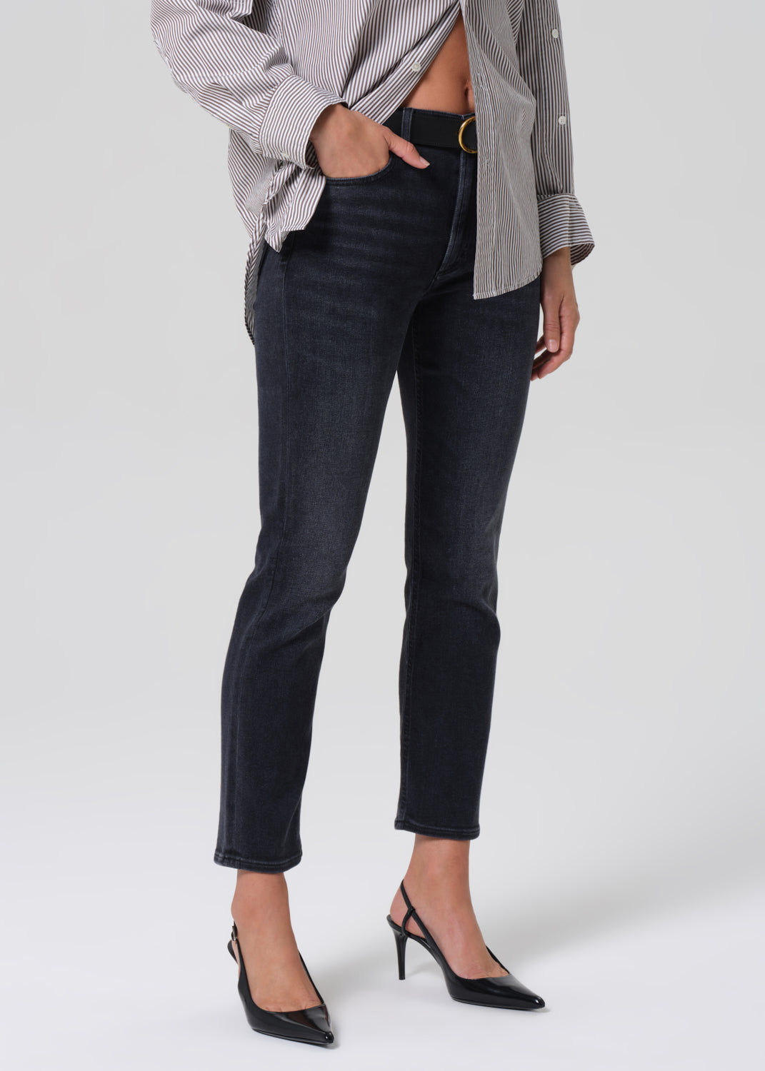 Person wearing a gray striped shirt and black jeans on a grey background