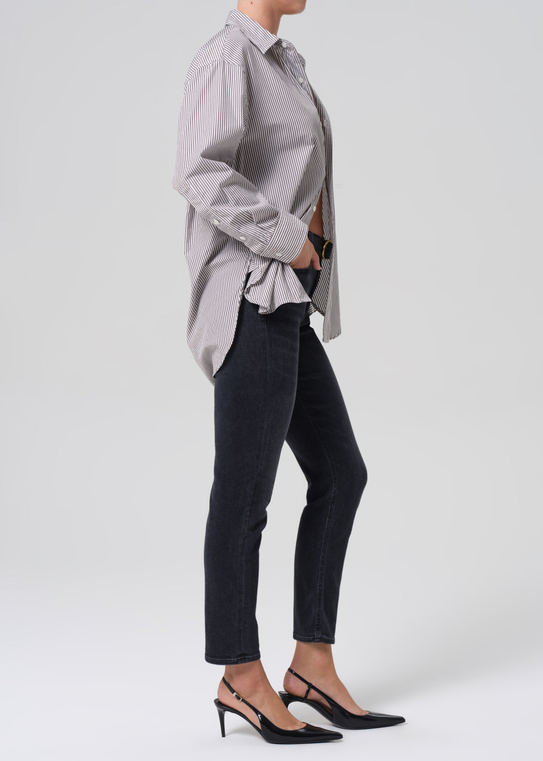 Person wearing a gray striped shirt and black jeans on a grey background