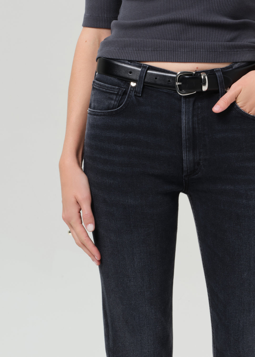 Person wearing a dark gray henley shirt and black jeans on a grey background