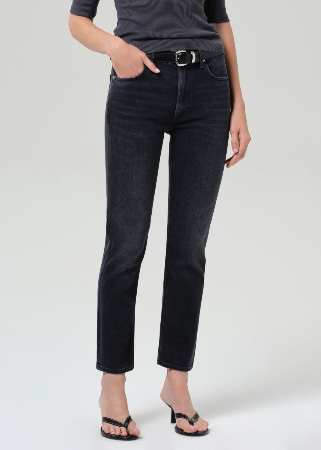 Person wearing a dark gray henley shirt and black jeans on a grey background