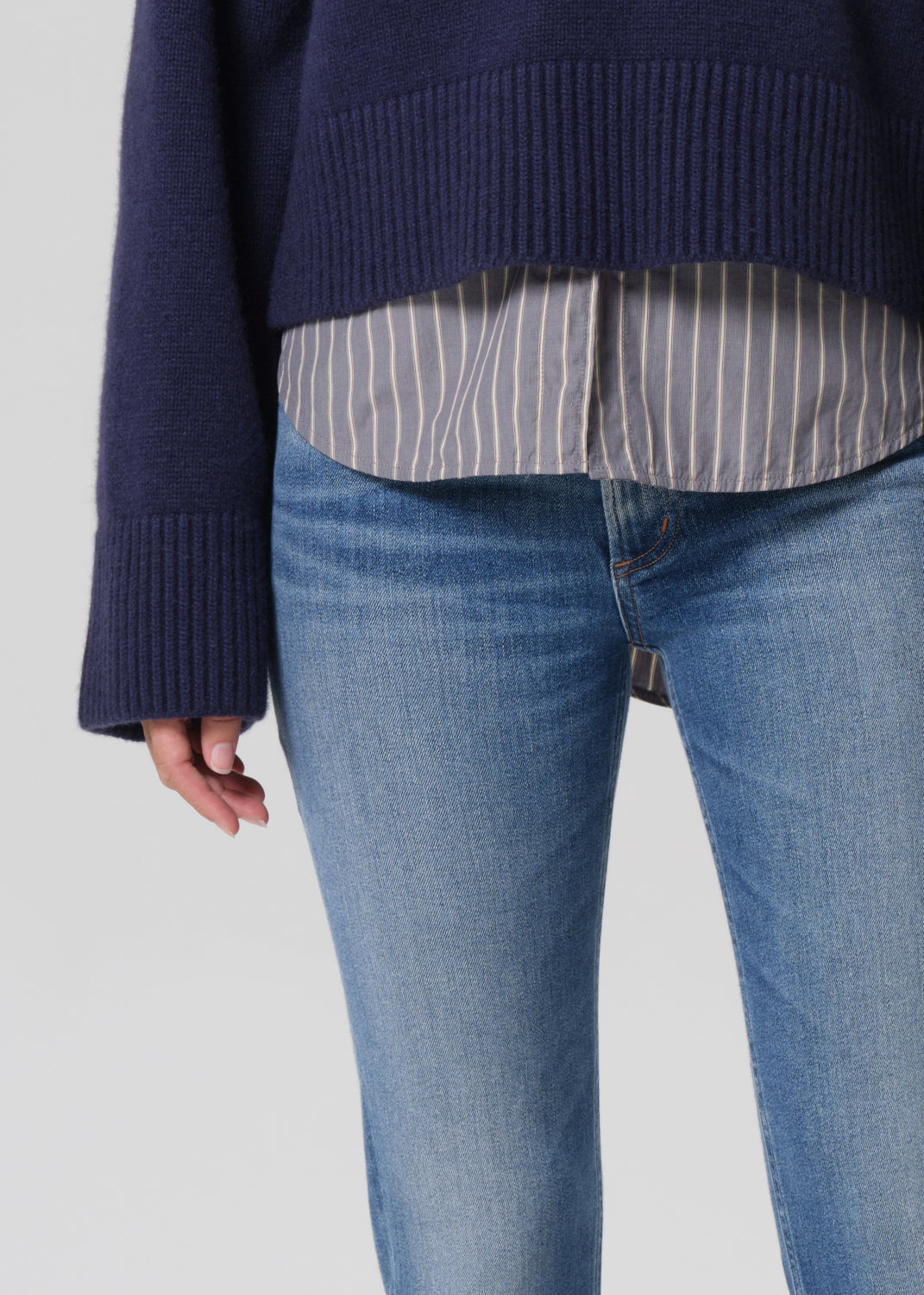 Navy sweater, striped shirt, and blue jeans on a plain background